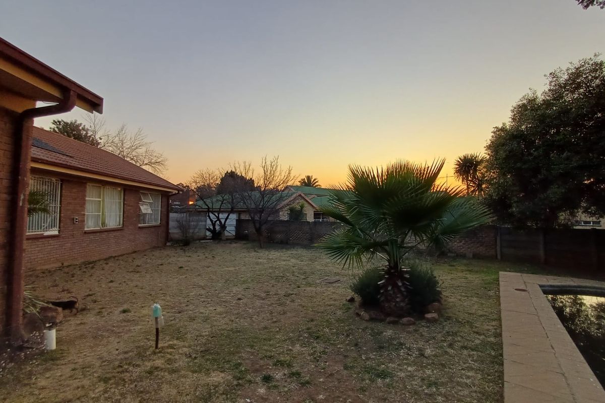 Rear exterior view of the property featuring a brick facade, tiled roof, swimming pool, and a spacious garden area at sunset.