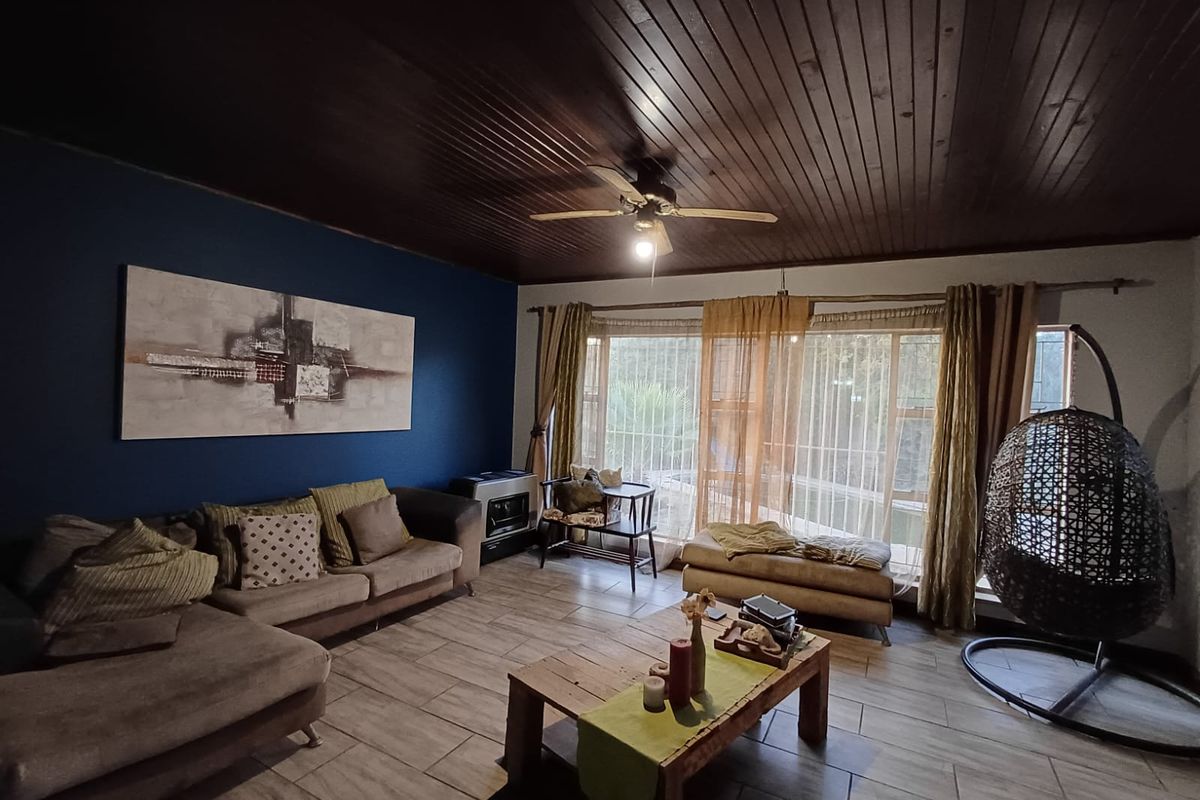A cozy living room featuring a dark timber-clad ceiling, tiled flooring, a large window for natural light, and a built-in fireplace.