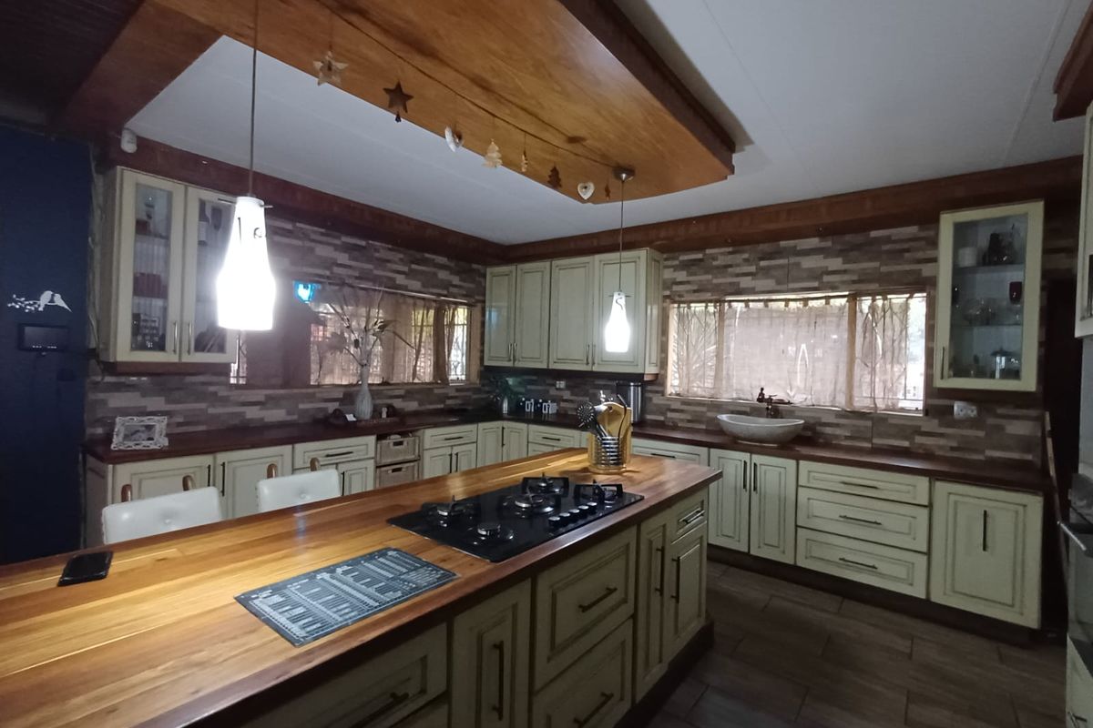 Spacious kitchen featuring a large central island with a built-in gas hob, wooden countertops, custom cabinetry, and a decorative timber ceiling feature.
