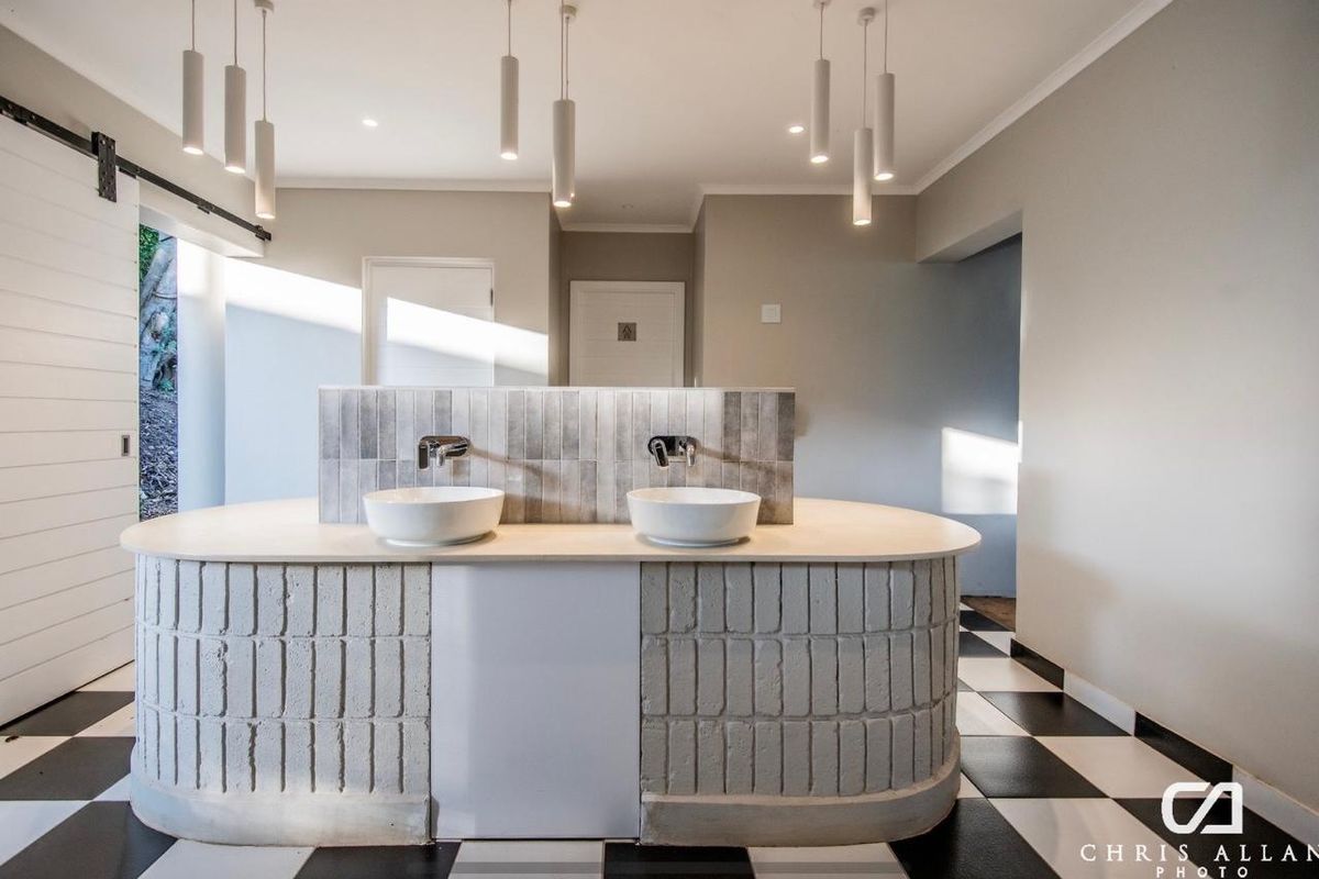 A modern bathroom featuring a unique curved double vanity with vessel sinks, wall-mounted faucets, and stylish checkered flooring.
