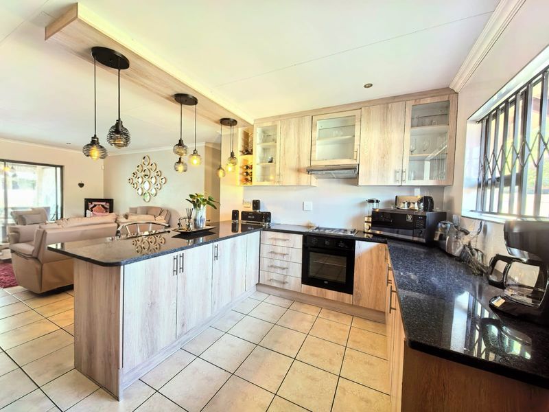 Open-plan kitchen featuring light wood-finish cabinetry, dark granite countertops, built-in oven, and hob, seamlessly flowing into the adjacent living area.