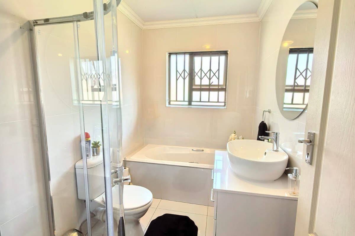 Modern bathroom featuring a curved glass shower enclosure, a built-in bathtub, a sleek vanity with a vessel sink, and tiled finishes throughout.