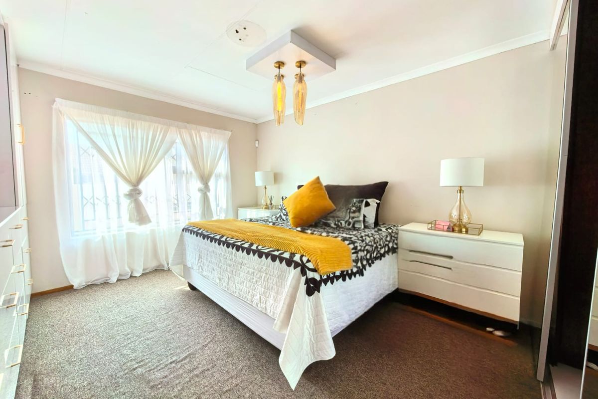 A well-lit bedroom featuring neutral walls, carpeted flooring, and a built-in wardrobe with modern handles.