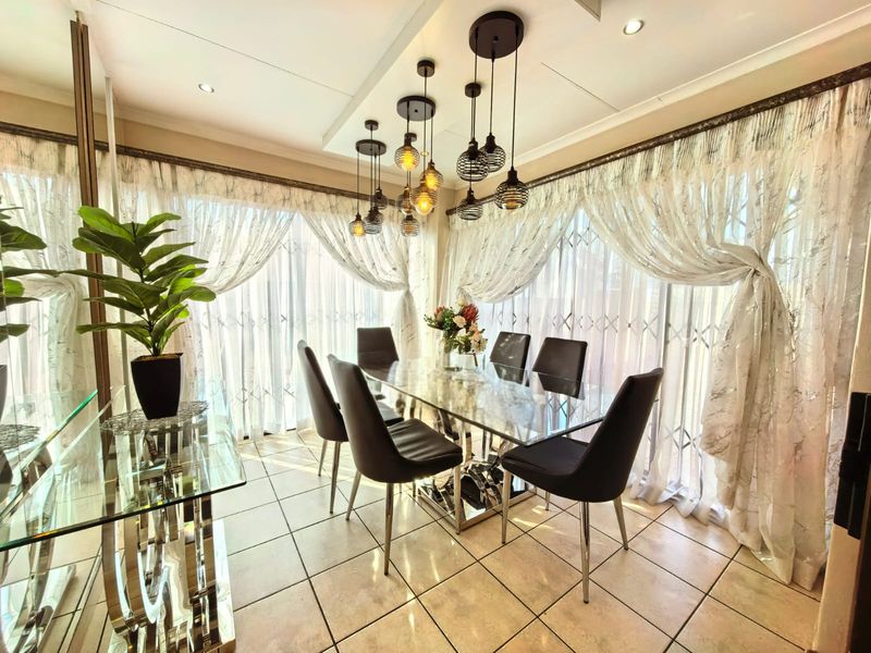 A bright dining room featuring tiled flooring, decorative pendant lighting, and large sliding glass doors with security gates providing ample natural light.