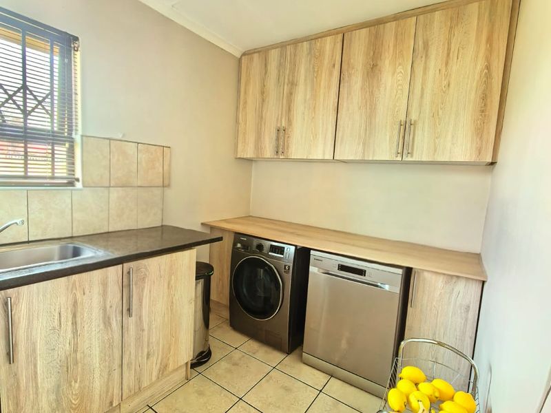 Functional laundry room featuring wood-look cabinetry, laminate countertops, tiled splashback, and tiled flooring with space for under-counter appliances.