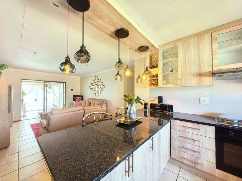Modern open-plan kitchen and living area featuring granite countertops, built-in appliances, light wood cabinetry, and direct access to an outdoor patio space.