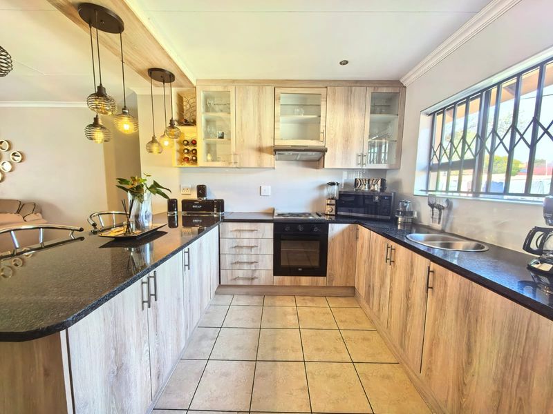 Modern kitchen featuring light wood-grain cabinetry, dark granite countertops, integrated appliances, and tiled flooring with a breakfast bar area.