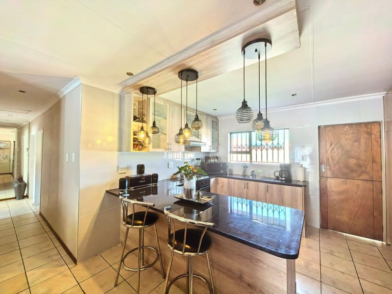 Modern kitchen featuring granite countertops, wood-look cabinetry, a breakfast bar, and stylish pendant lighting, complemented by tiled flooring and secure window fixtures.