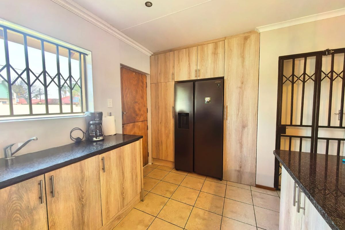 A functional kitchen featuring light wood-grain cabinetry, dark granite countertops, tiled flooring, and integrated security features on windows and doors.