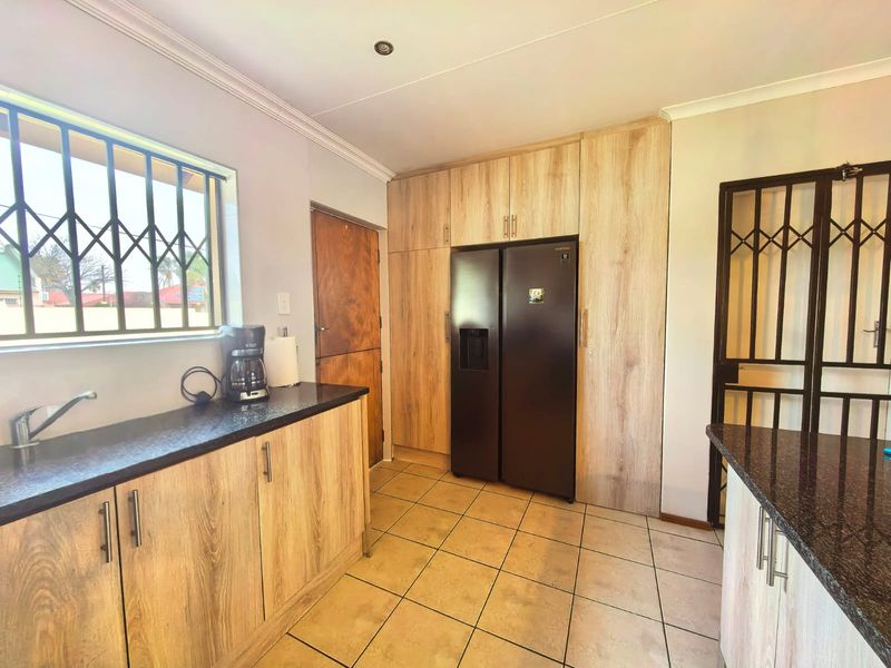 A functional kitchen featuring light wood-grain cabinetry, dark granite countertops, tiled flooring, and integrated security features on windows and doors.