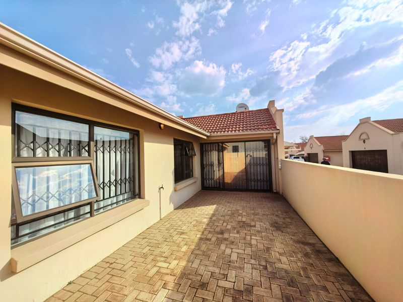 A private paved rear patio area featuring secure metal gates, tiled roofing, and a boundary wall, providing a functional outdoor space.