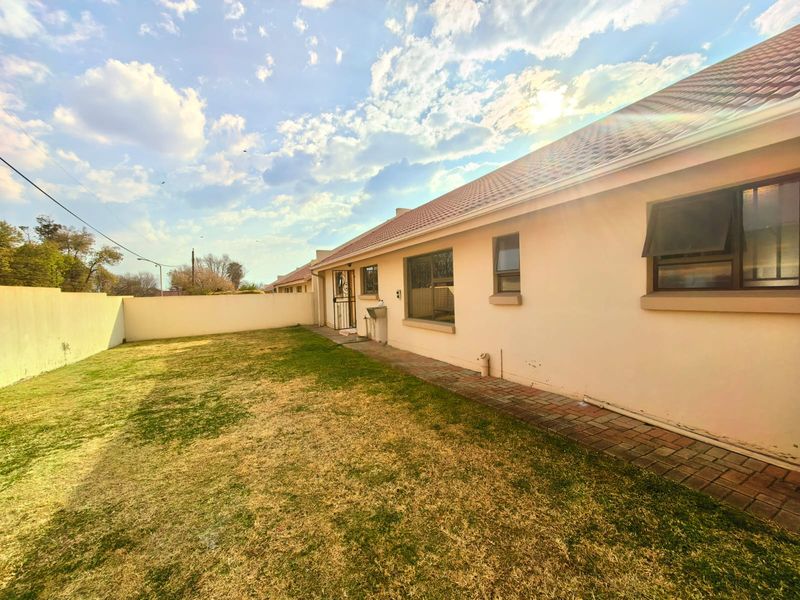 Rear exterior view of the townhouse featuring a private garden, paved walkway, perimeter wall, and external wash basin.