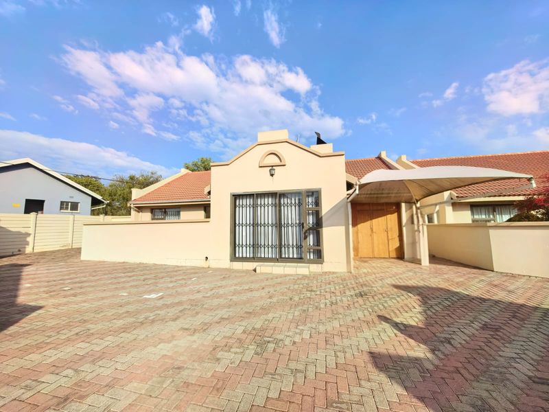 Front exterior view of a townhouse featuring a paved driveway, tiled roof, and a covered parking area with a shade sail.