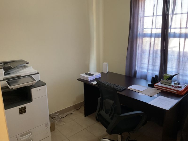 A functional home office space featuring tiled flooring and a window with curtains, providing a practical area for work or study.