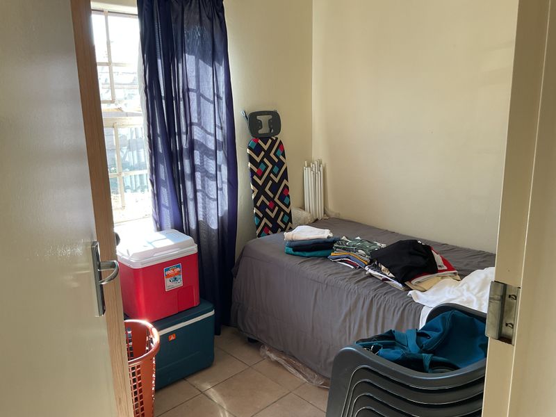 A compact bedroom featuring tiled flooring and a window, currently utilized as a multi-purpose storage and sleeping space.
