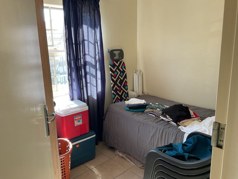 A compact bedroom featuring tiled flooring and a window with security bars, providing a functional space for a single bed.