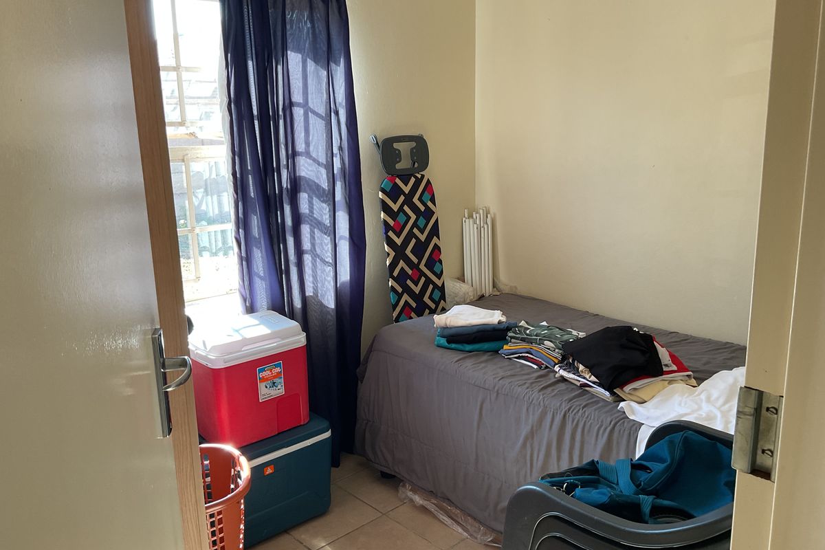 A compact bedroom featuring tiled flooring and a window with security bars, providing a functional space for a single bed.