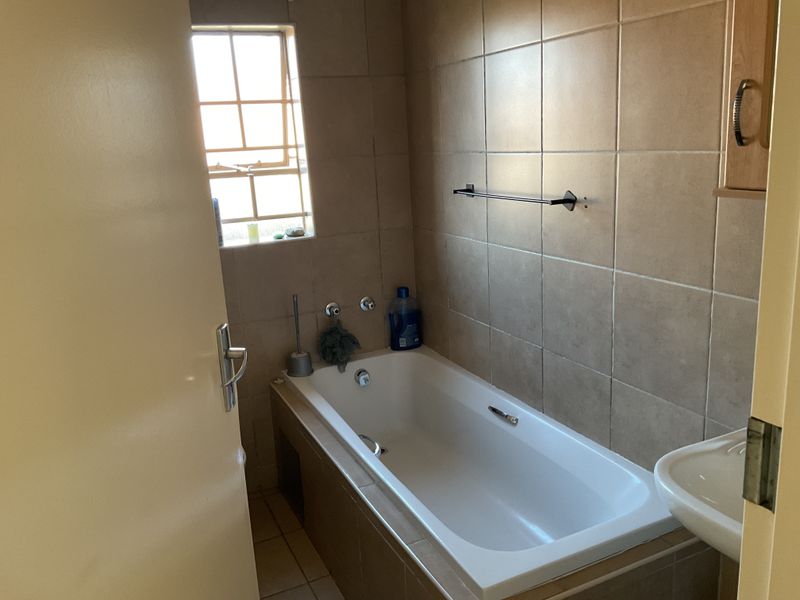 A functional bathroom featuring a built-in bathtub, tiled wall finishes, and a wall-mounted basin, providing a practical layout for daily use.