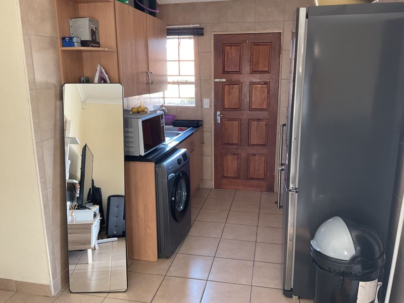 A functional laundry area featuring tiled flooring, laminate cabinetry, and a timber exterior door, providing practical utility space for the home.