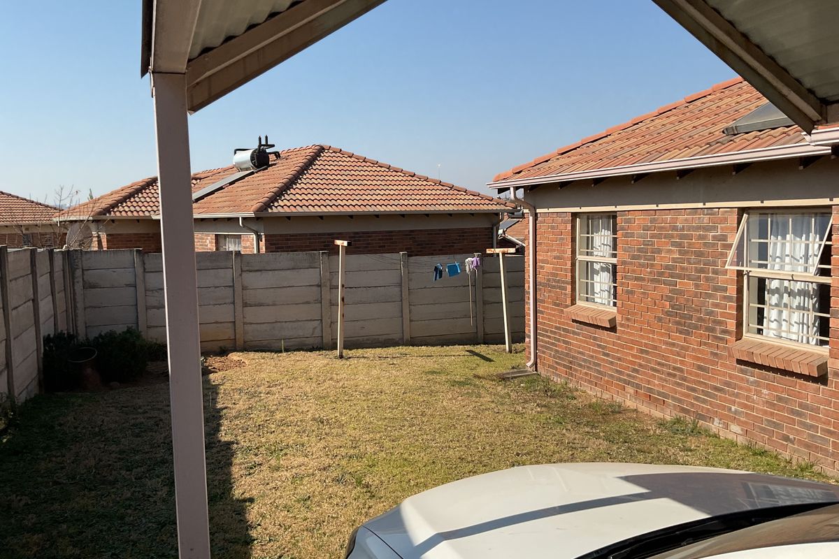 A rear exterior view of the property featuring a brick facade, corrugated metal roof, solar water heater, and a private garden area with boundary wall.