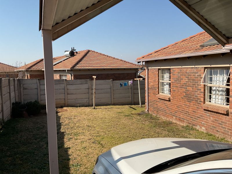 A rear exterior view of the property featuring a brick facade, corrugated metal roof, solar water heater, and a private garden area with boundary wall.