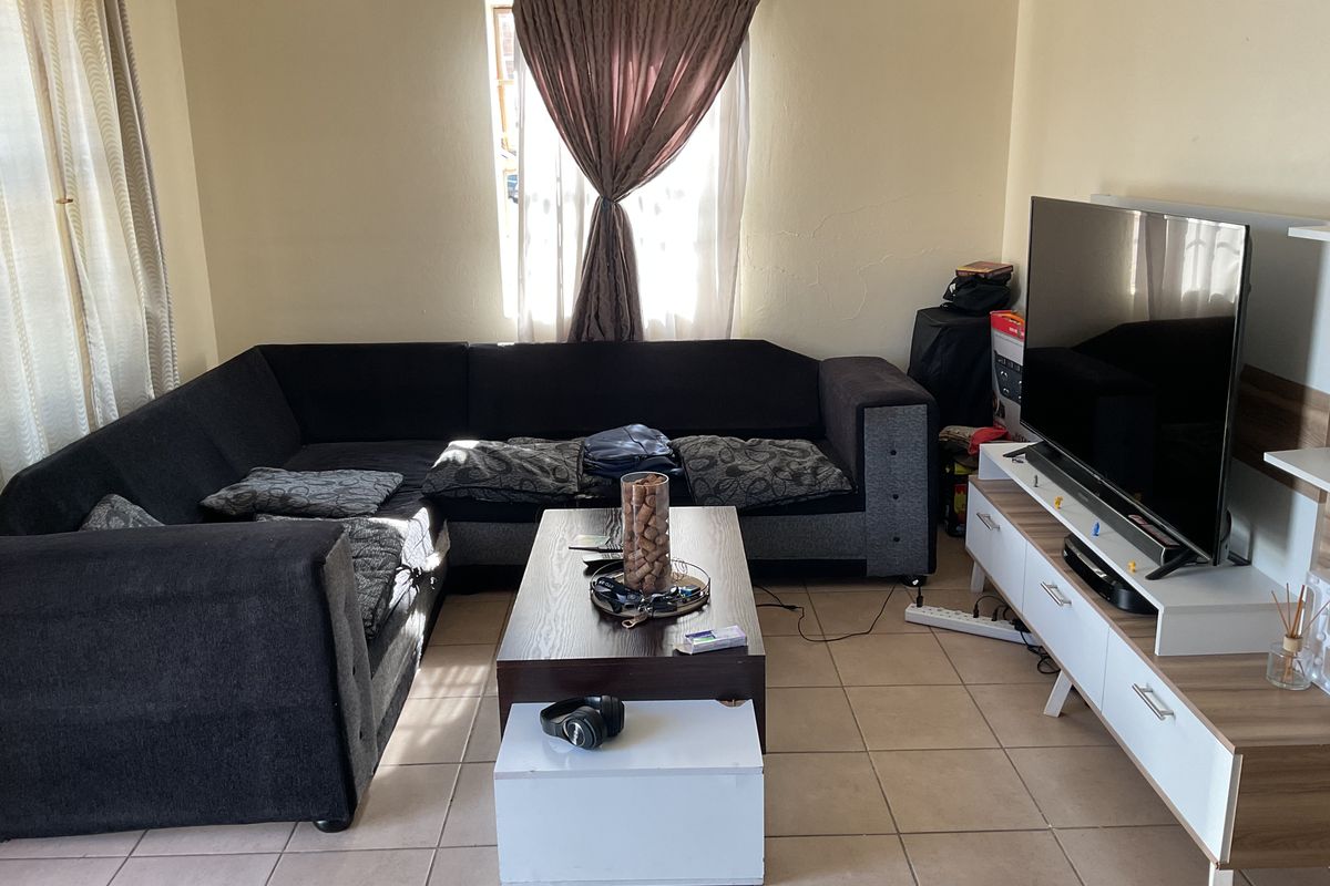 A functional living room featuring tiled flooring and natural light from a window, providing a comfortable space for relaxation.