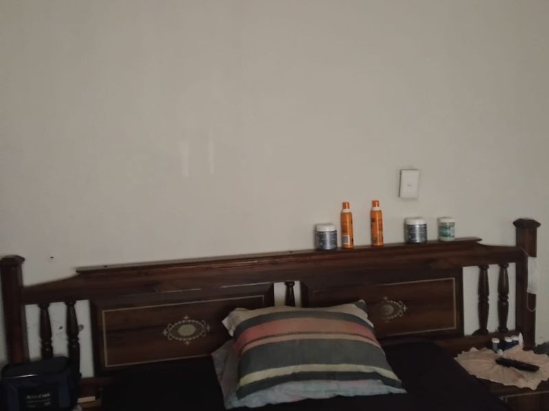 A bedroom interior featuring a wooden headboard and a wall-mounted light switch.