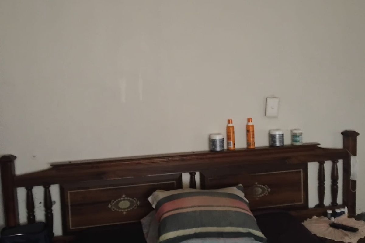 A bedroom interior featuring a wooden headboard and a wall-mounted light switch.