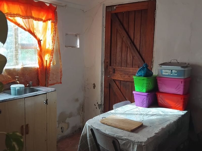 A compact kitchen area featuring a stainless steel sink, basic cabinetry, and a timber door, requiring significant cosmetic updates and wall repairs.