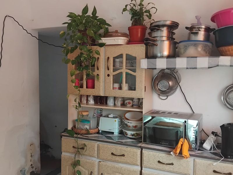 A dated kitchen area featuring laminate cabinetry and built-in shelving, currently showing signs of wear and wall surface damage.