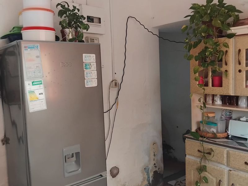 A kitchen area featuring built-in cabinetry and an electrical distribution board, showing signs of wall dampness and exposed wiring requiring maintenance.