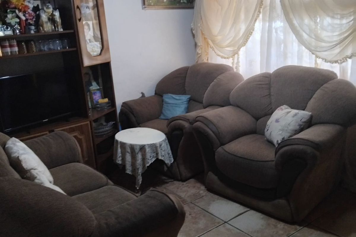 A living room area featuring ceramic floor tiles and a window with draped curtains.