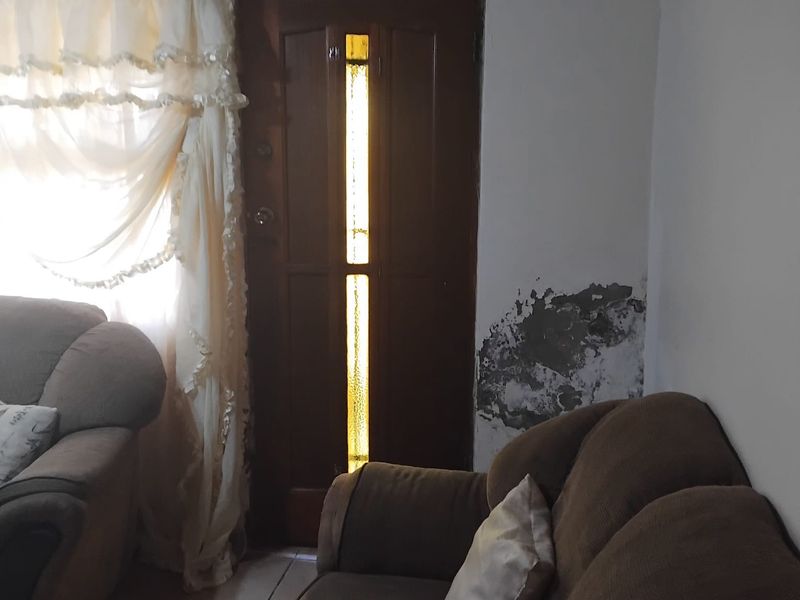 Living room area featuring a timber door and tiled flooring, currently showing significant wall plaster damage and peeling paint requiring maintenance.