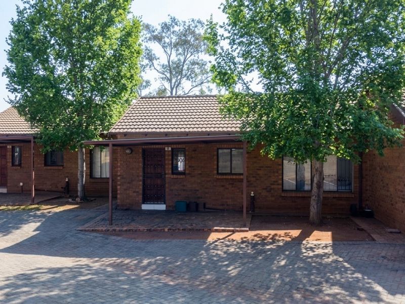 Front view of a brick townhouse featuring a covered patio, paved driveway, and secure entrance with security gates and bars.