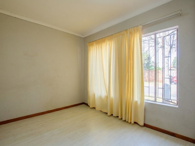 An empty bedroom featuring laminate flooring, neutral walls, and a window fitted with security bars.