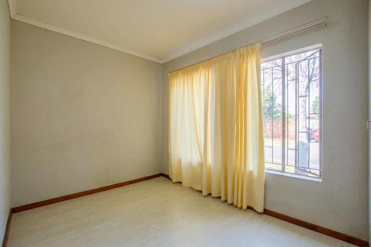An empty bedroom featuring laminate flooring, neutral walls, and a window fitted with security bars.