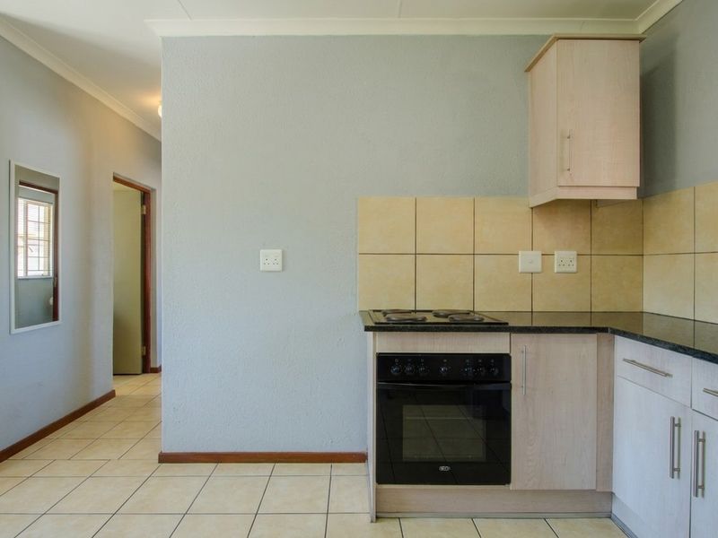 A functional kitchen area featuring light wood cabinetry, granite countertops, a built-in oven and hob, and neutral tiled flooring.