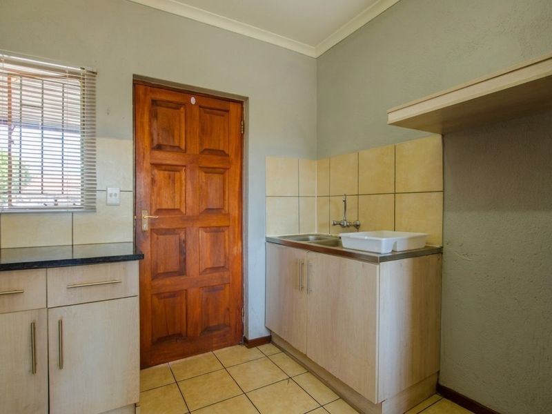 A functional laundry area featuring built-in cabinetry, a stainless steel sink, tiled splashback, and direct access to the exterior.
