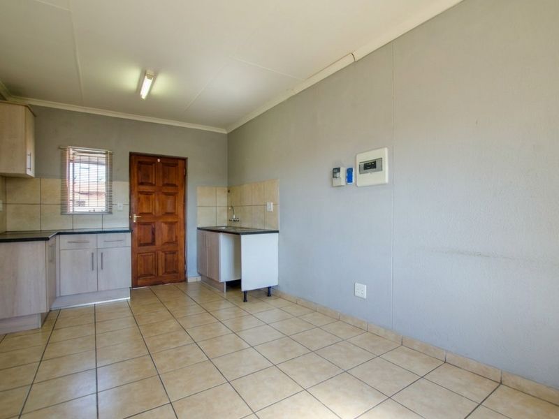 A compact, empty kitchen area featuring tiled flooring, built-in cabinetry with laminate countertops, and a tiled splashback.