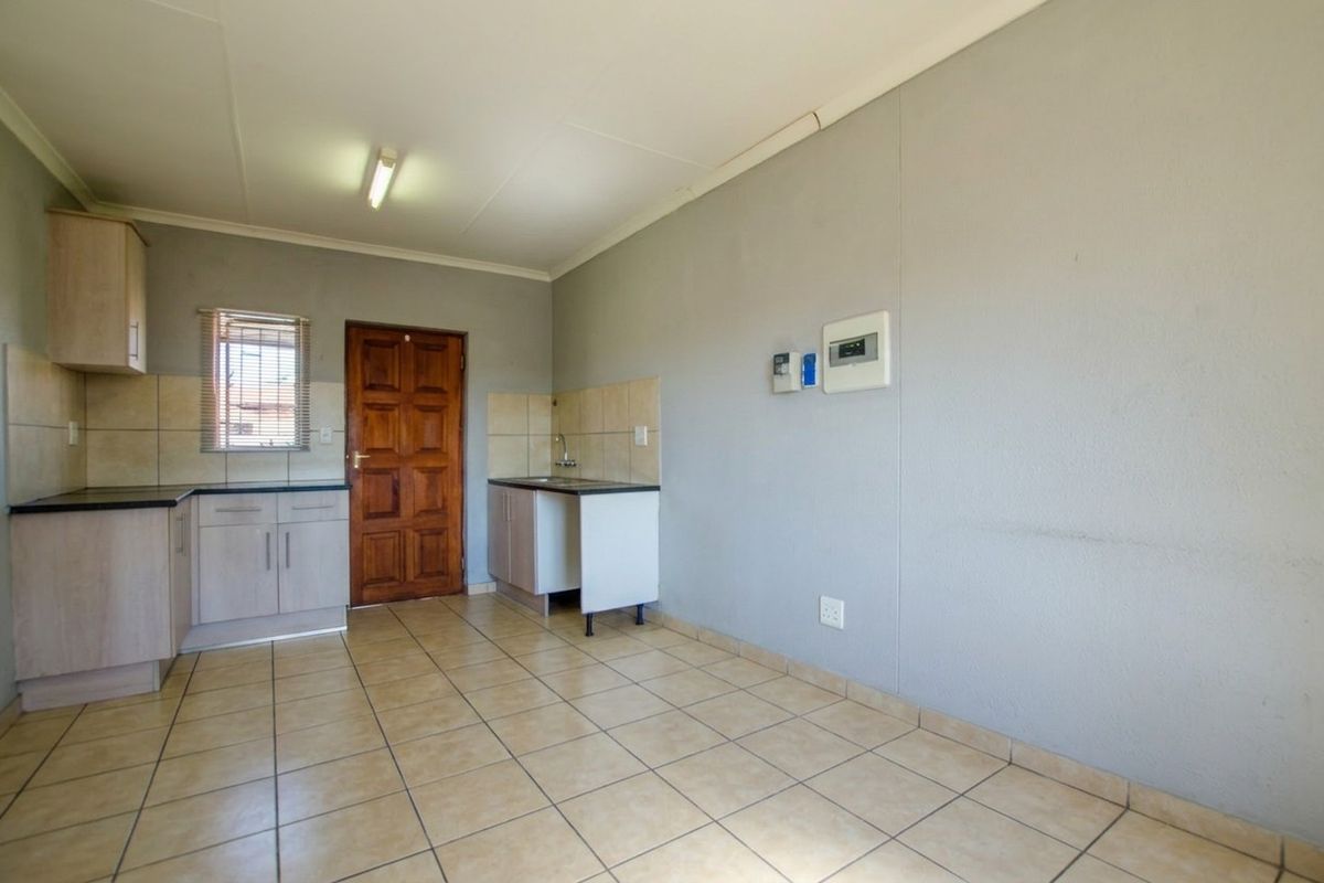 A compact, empty kitchen area featuring tiled flooring, built-in cabinetry with laminate countertops, and a tiled splashback.