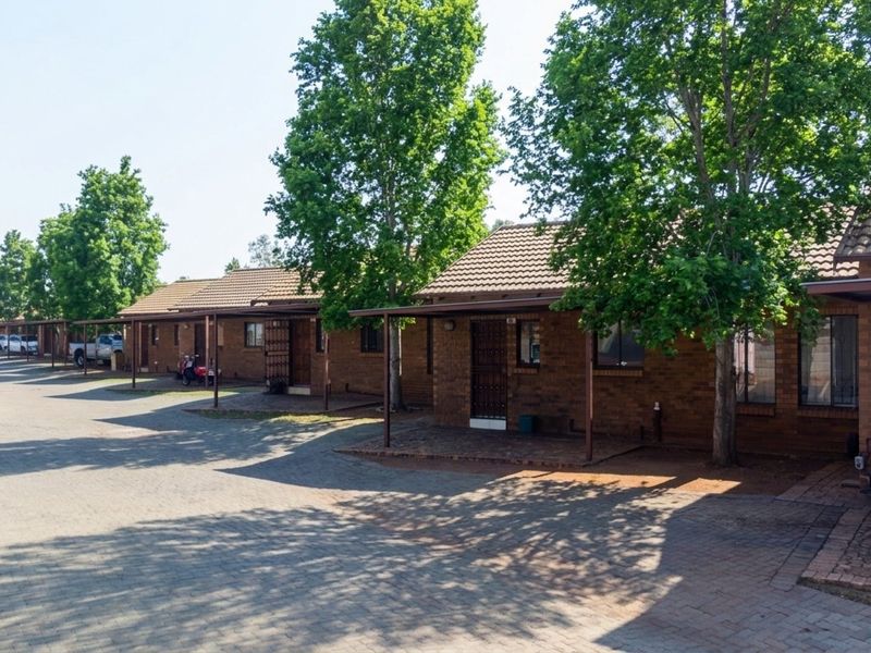 A row of single-story brick townhouses featuring tiled roofs, paved driveway access, and covered walkways with security gates.