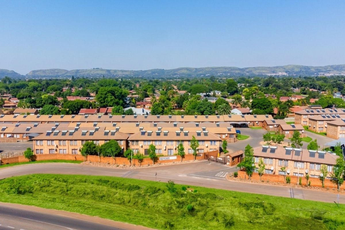 Aerial view of a townhouse complex featuring multiple units with tiled roofs, solar water heaters, and secure perimeter walling.