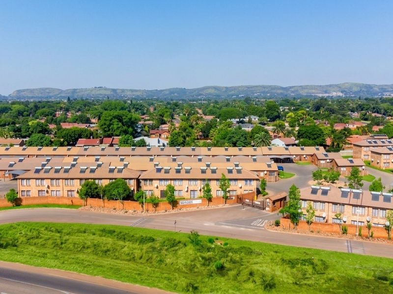 Aerial view of a townhouse complex featuring multiple units with tiled roofs, solar water heaters, and secure perimeter walling.