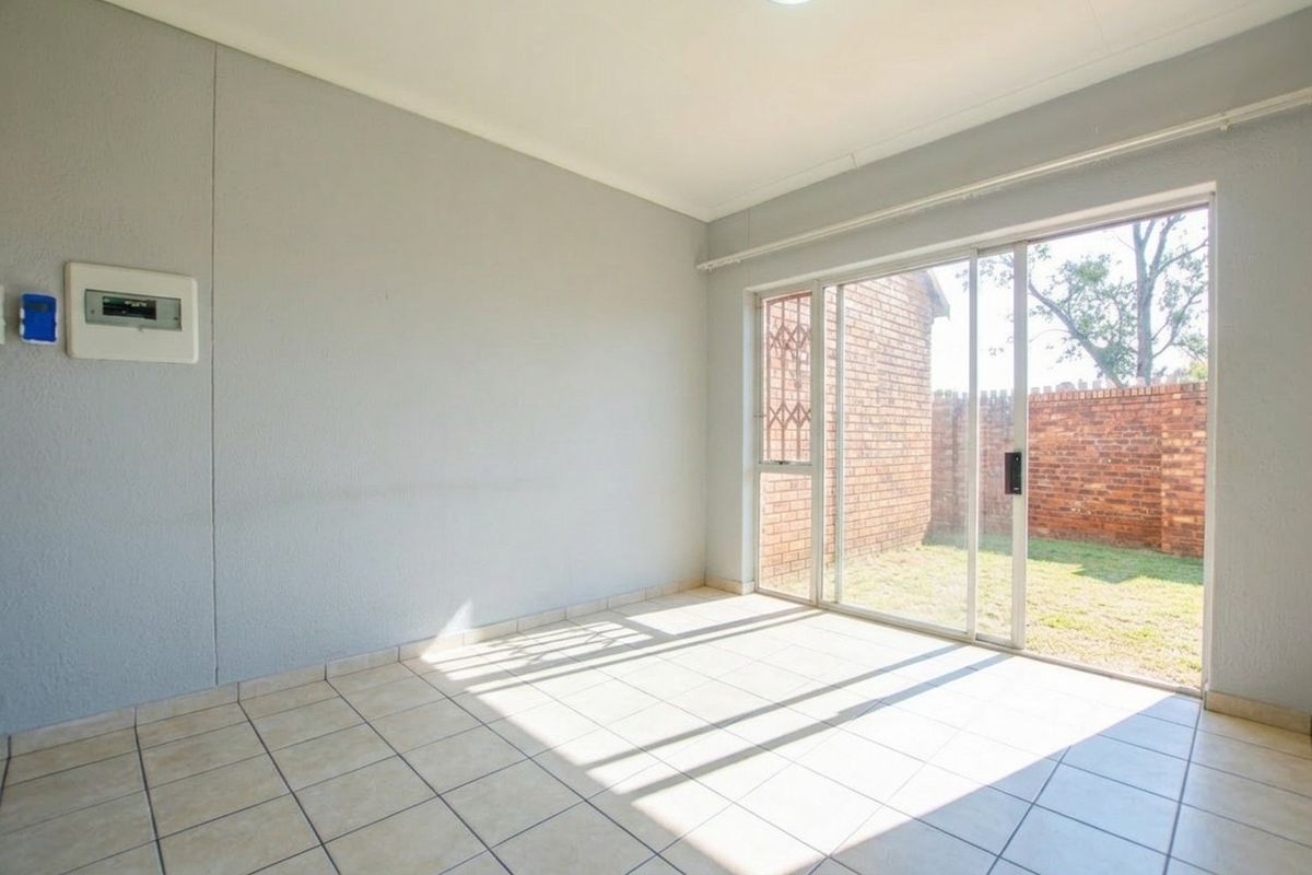 An empty living room featuring tiled flooring and a large sliding glass door providing direct access to the rear garden area.