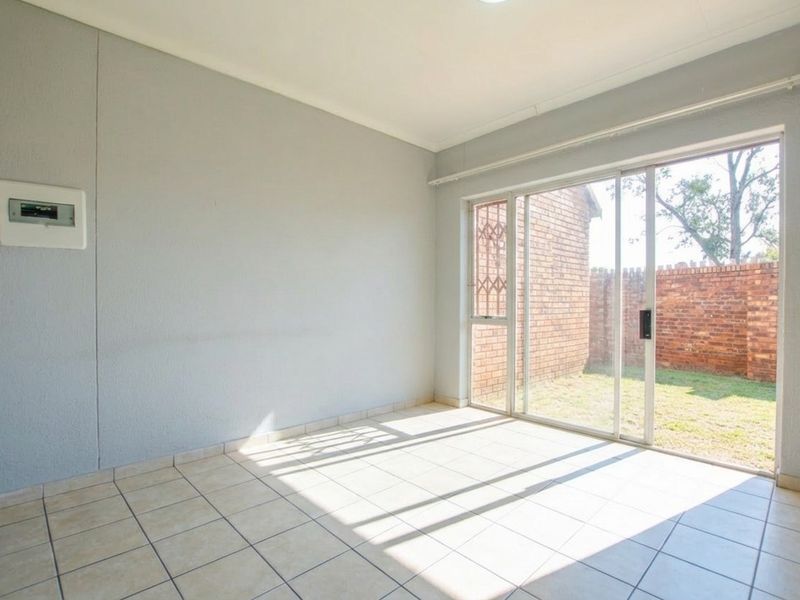 An empty living room featuring tiled flooring and a large sliding glass door providing direct access to the rear garden area.