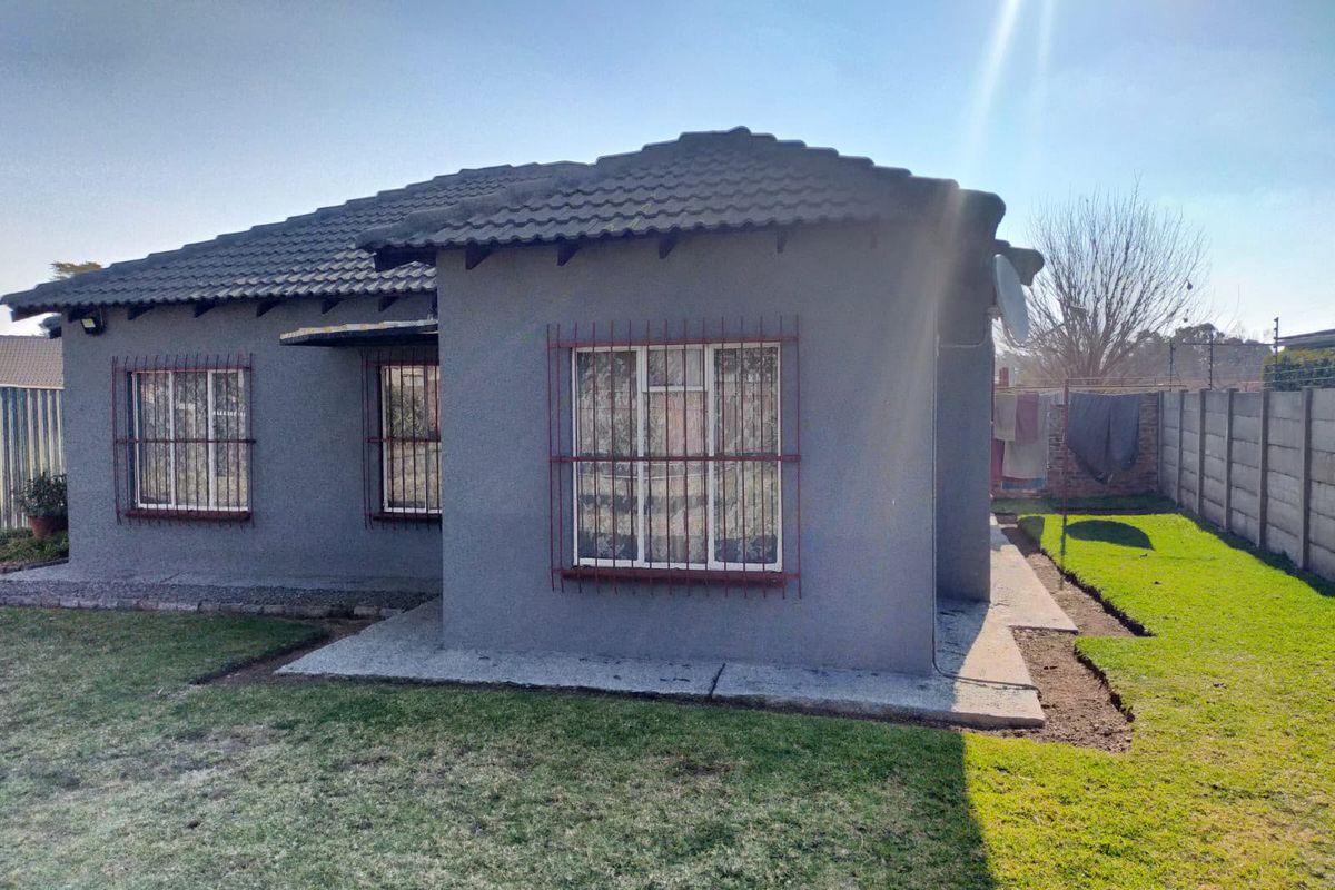 Rear view of a single-story house featuring a tiled roof, security bars on windows, and a surrounding garden with a precast concrete boundary wall.