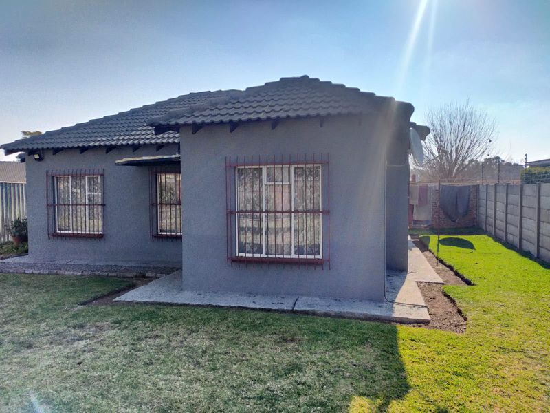 Rear view of a single-story house featuring a tiled roof, security bars on windows, and a surrounding garden with a precast concrete boundary wall.