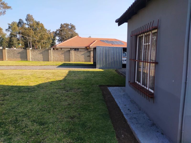 Rear exterior view showing a lawn, perimeter wall, metal storage shed, and a building facade with security bars on the windows.