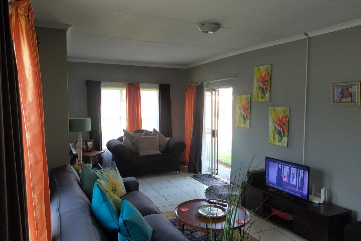 A living room featuring tiled flooring, neutral grey walls, and a sliding glass door providing access to the exterior.