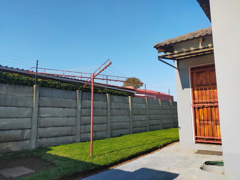A rear exterior view showing a lawn area, precast concrete boundary wall with electric fencing, and a rotary clothesline.